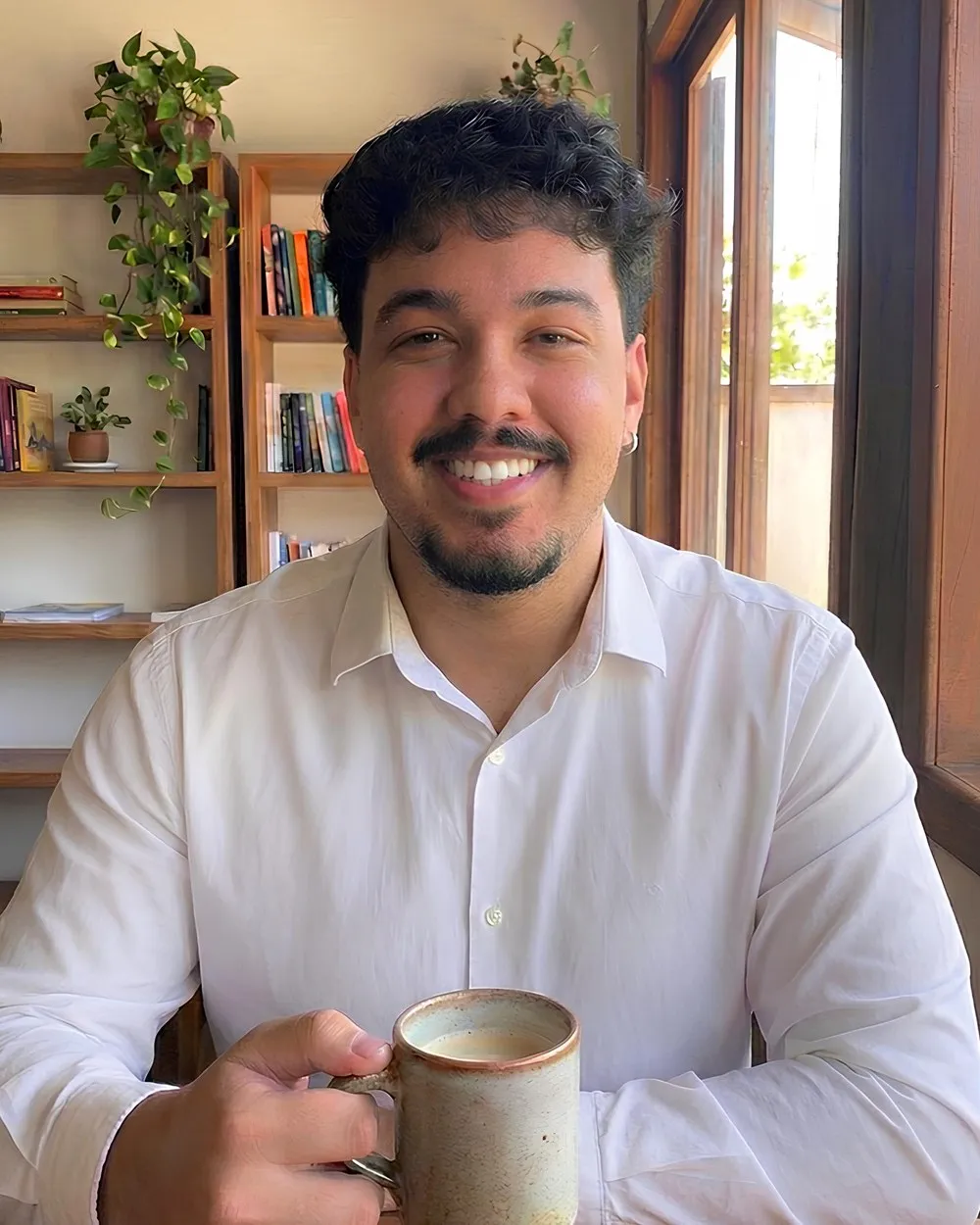 Marco Fabian sorrindo, de camisa branca, segurando uma caneca de café